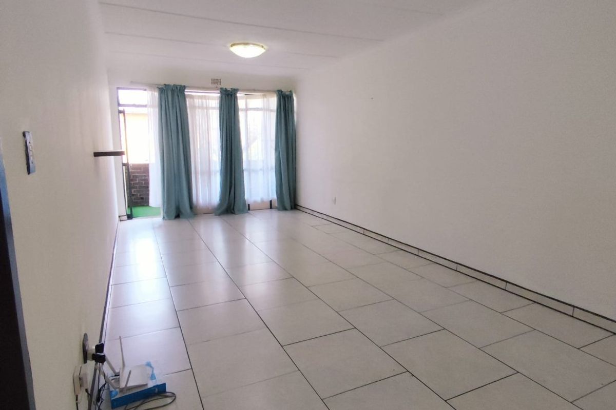 A spacious, empty living area featuring neutral tiled flooring, bright white walls, and a sliding glass door leading to an outdoor space.