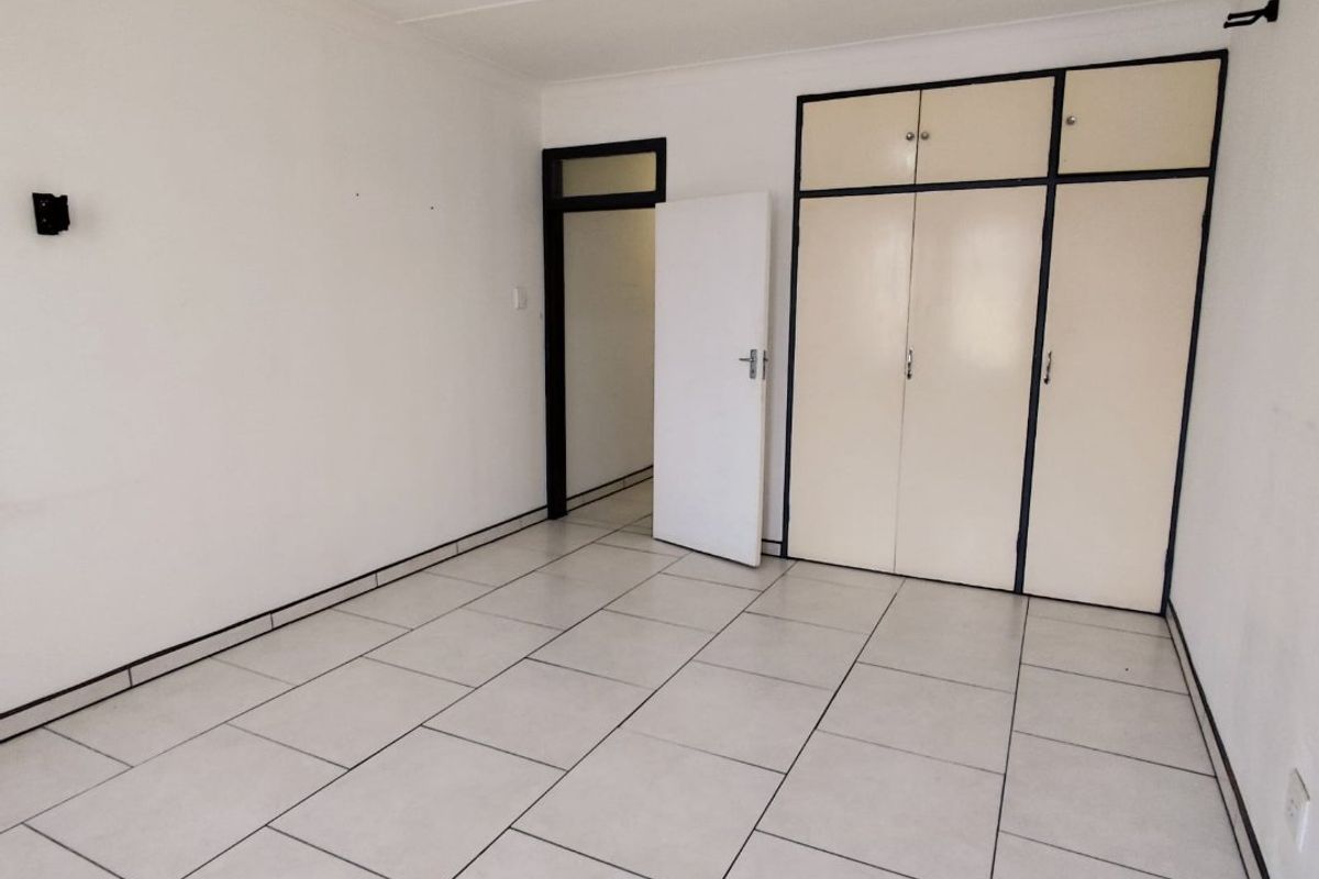 An empty bedroom featuring tiled flooring and built-in cupboards with a neutral color palette, ready for personalization.