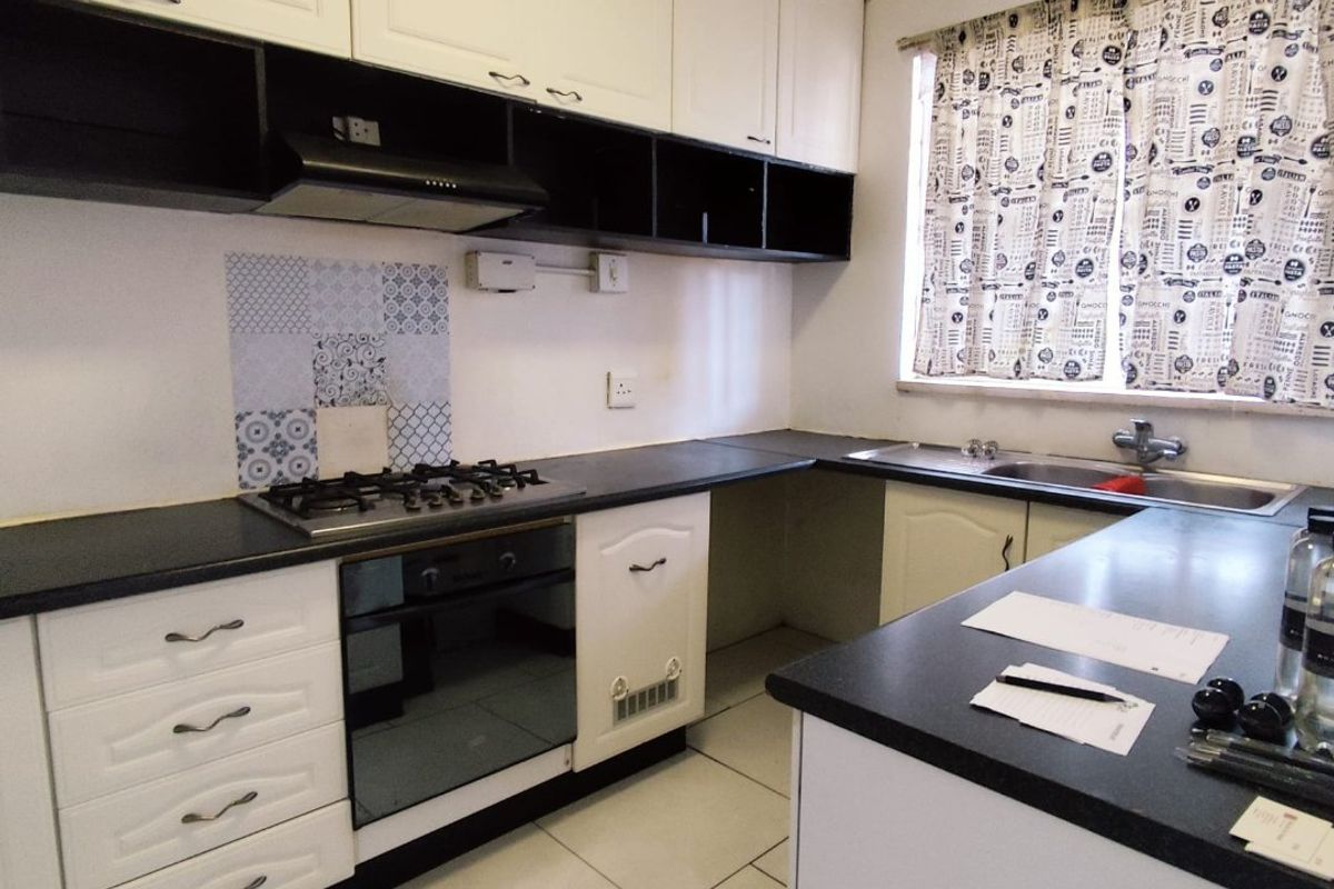 A functional kitchen featuring white cabinetry, dark countertops, a gas hob with extractor, and a stainless steel sink with tiled flooring.