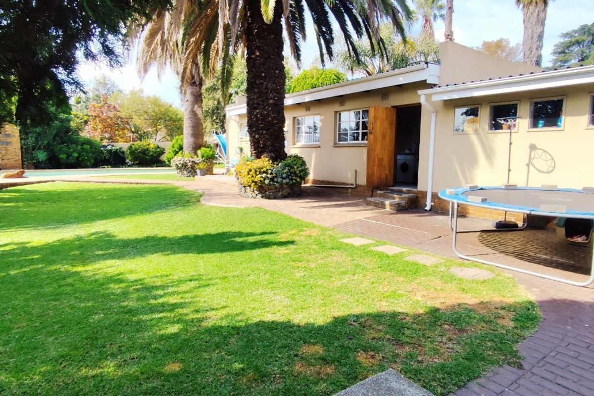Spacious rear garden featuring a well-maintained lawn, mature palm trees, and a paved patio area adjacent to the house exterior.