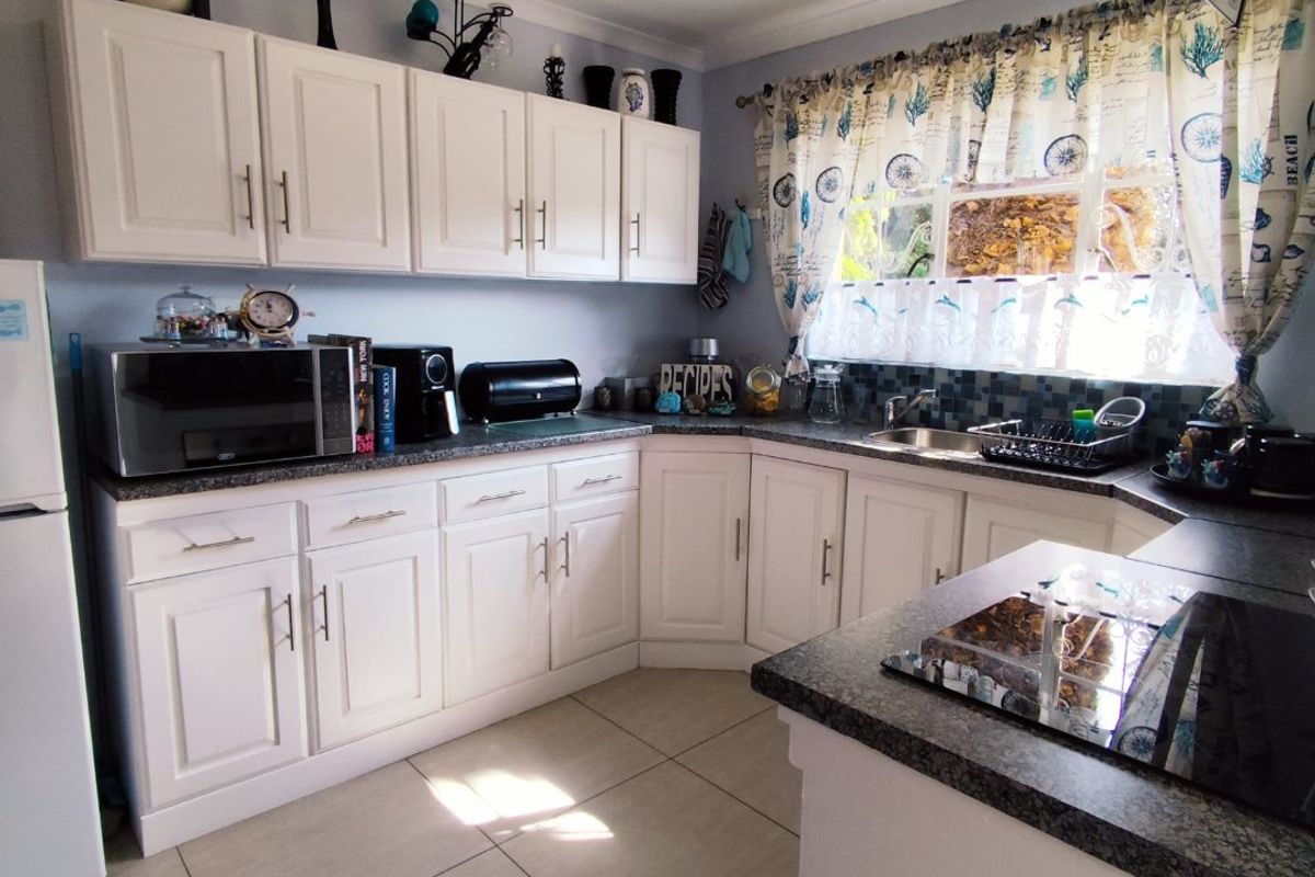 A functional kitchen featuring white cabinetry, dark granite-style countertops, tiled flooring, and a built-in glass cooktop with an overhead extractor fan.