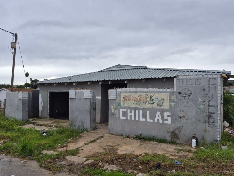 Front exterior view of a commercial property featuring a corrugated metal roof and masonry boundary wall with painted signage.