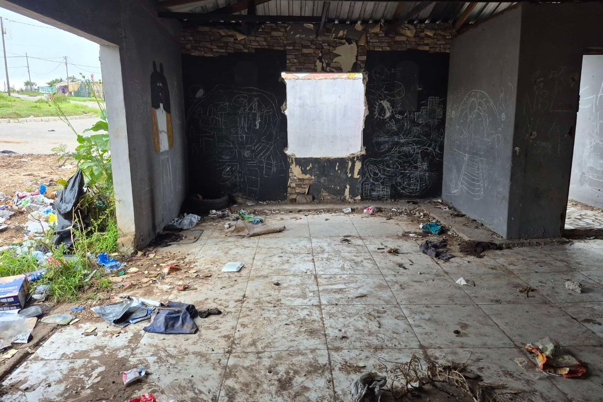 An empty, dilapidated interior space featuring tiled flooring and exposed roof structure, requiring significant renovation and repair to restore functionality.