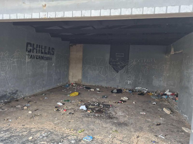 An empty, neglected commercial space featuring concrete flooring and walls covered in graffiti, requiring significant refurbishment and cleaning.