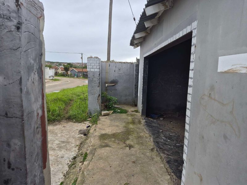 Exterior view of a commercial property showing a concrete pathway, boundary wall, and unfinished building structure with visible wear and weathering.