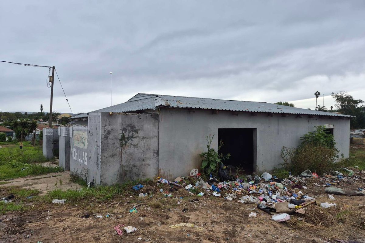 Rear view of a commercial structure featuring concrete block walls and a corrugated metal roof, showing significant signs of neglect and exterior damage.