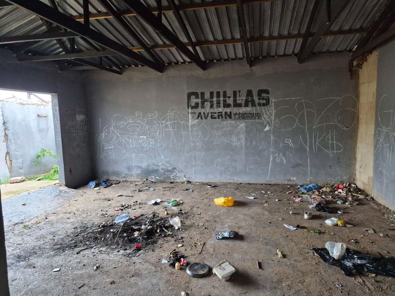 An unfinished commercial interior space featuring exposed metal roof trusses, concrete flooring, and graffiti-covered walls, requiring significant renovation and cleanup.