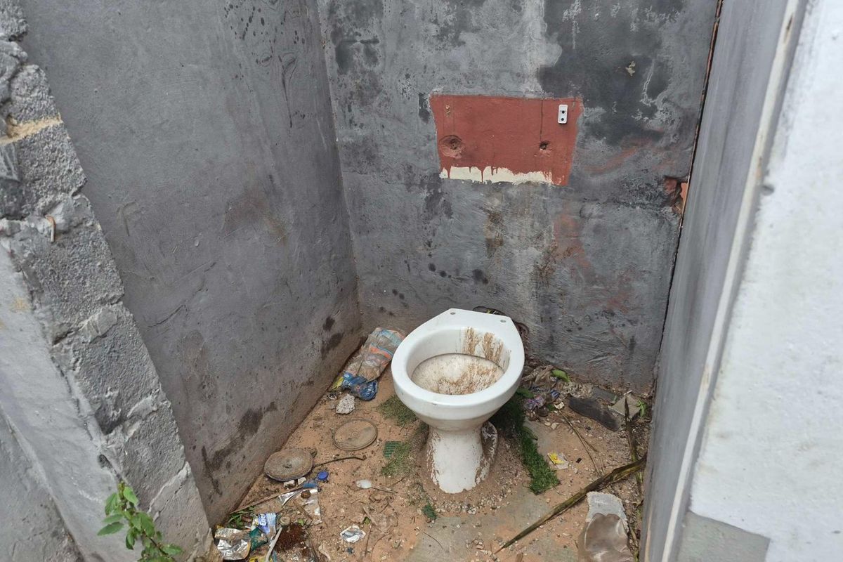 A severely dilapidated bathroom space featuring an exposed concrete shell and a heavily soiled toilet, requiring extensive renovation and cleaning.