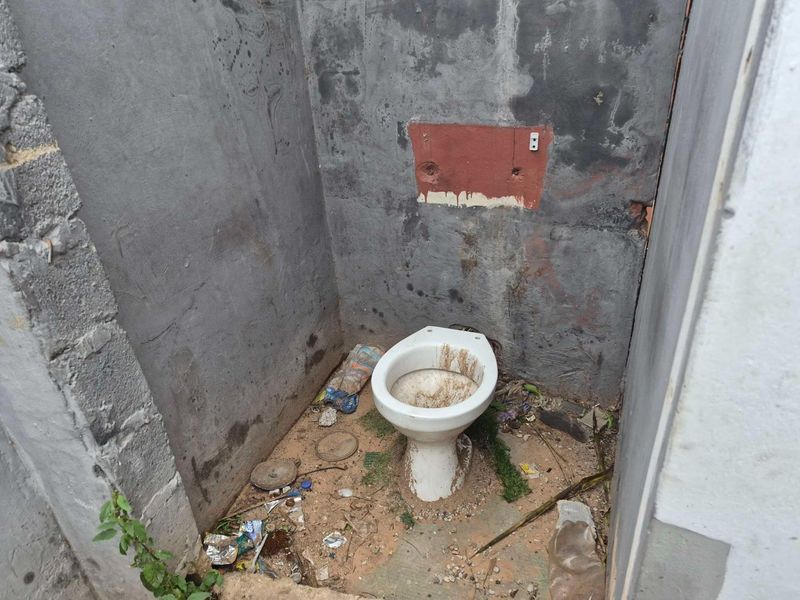 A severely dilapidated bathroom space featuring an exposed concrete shell and a heavily soiled toilet, requiring extensive renovation and cleaning.