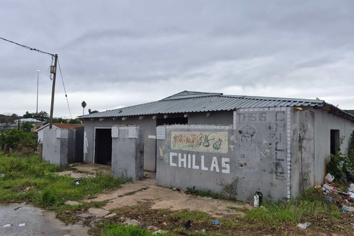 Exterior view of a commercial property featuring a corrugated metal roof and masonry boundary walls, showing significant signs of wear and exterior weathering.