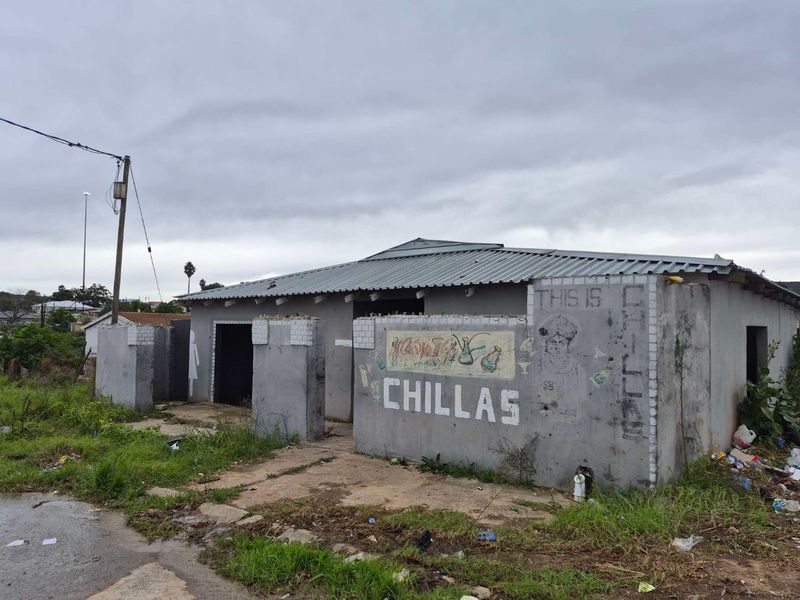 Exterior view of a commercial property featuring a corrugated metal roof and masonry boundary walls, showing significant signs of wear and exterior weathering.