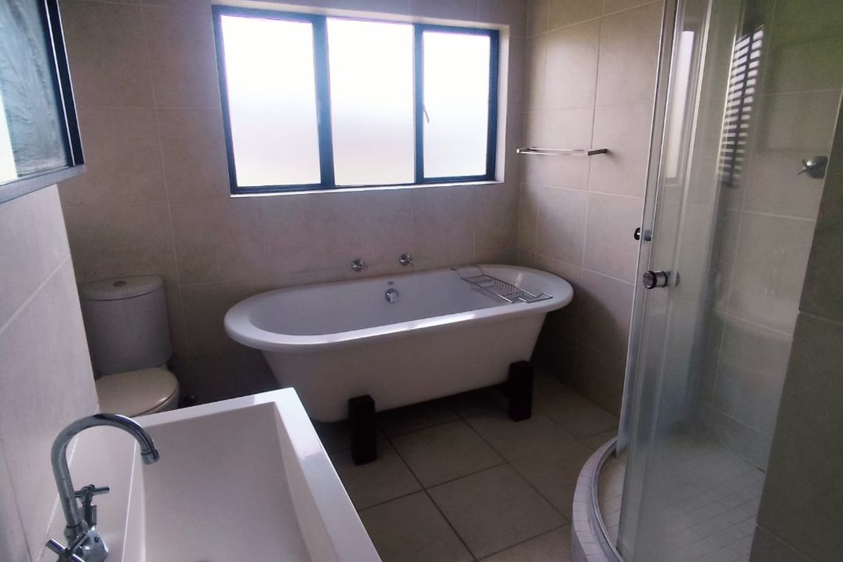 A well-appointed bathroom featuring a freestanding bathtub, a separate glass-enclosed shower, a modern basin, and neutral floor-to-ceiling tiling.