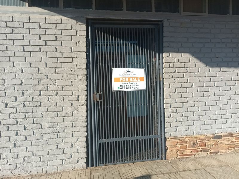 Commercial building entrance featuring a metal security gate, painted brick exterior, and stone cladding base, currently marked with a for sale sign.