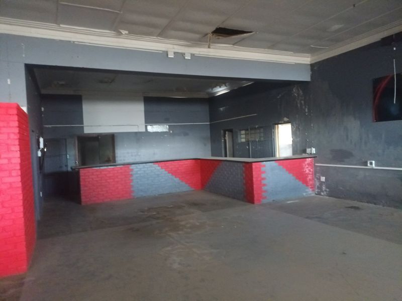 An empty commercial bar area featuring a built-in brick counter, security grilles, and significant wear to the ceiling and wall finishes.