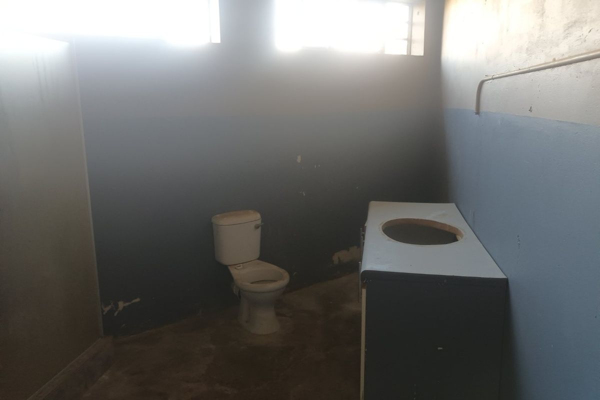 A vacant bathroom space featuring a toilet and vanity cabinet, requiring significant renovation and cosmetic updates to restore functionality and aesthetic appeal.