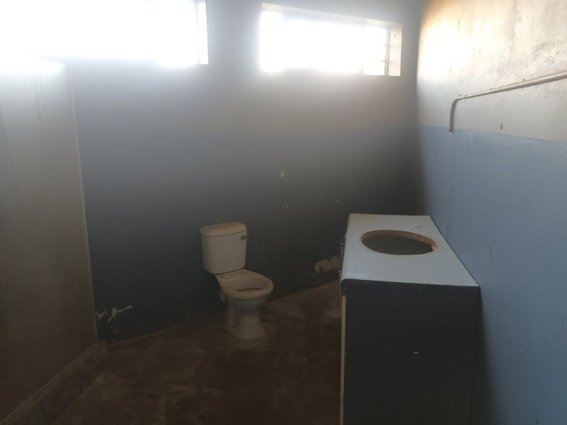 A vacant bathroom space featuring a toilet and vanity cabinet, requiring significant renovation and cosmetic updates to restore functionality and aesthetic appeal.