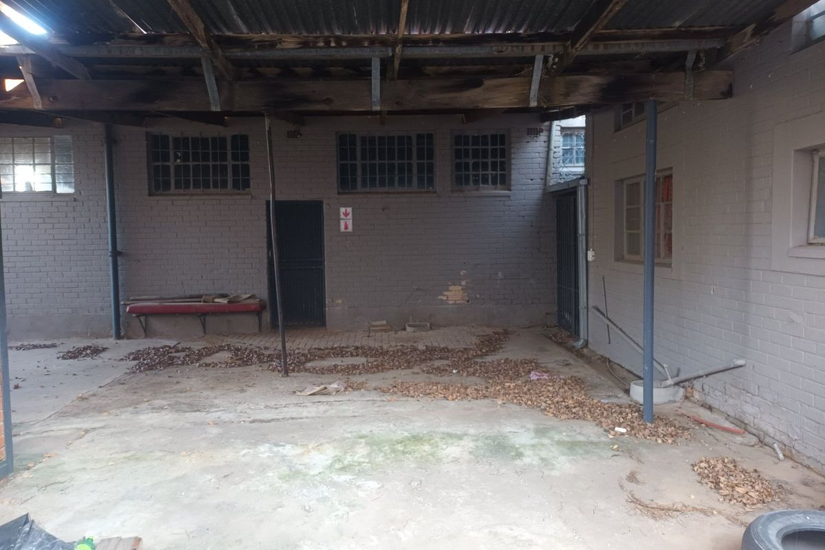 A covered outdoor utility or rear courtyard area featuring exposed timber rafters, corrugated iron roofing, and brick masonry walls in need of maintenance.