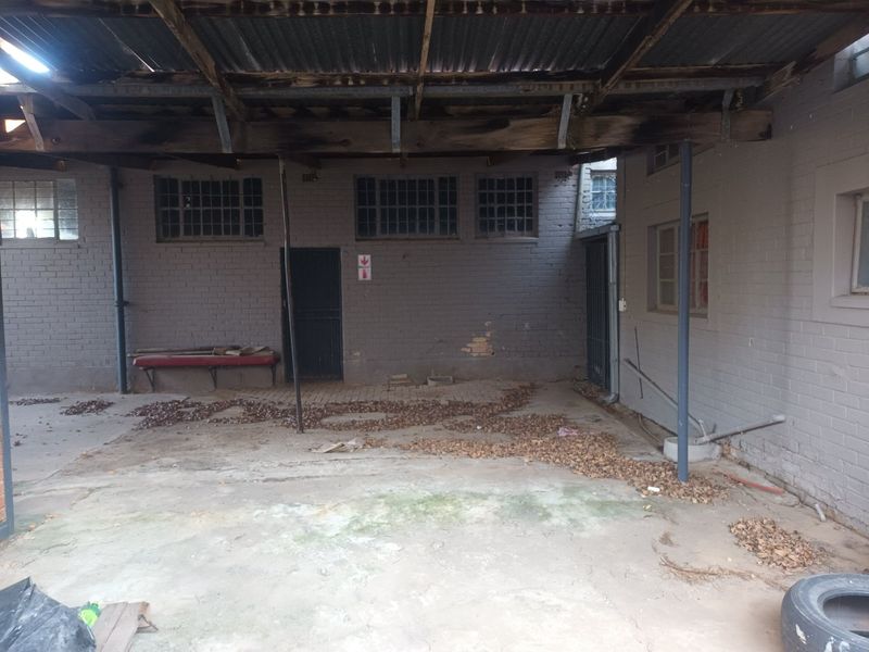 A covered outdoor utility or rear courtyard area featuring exposed timber rafters, corrugated iron roofing, and brick masonry walls in need of maintenance.