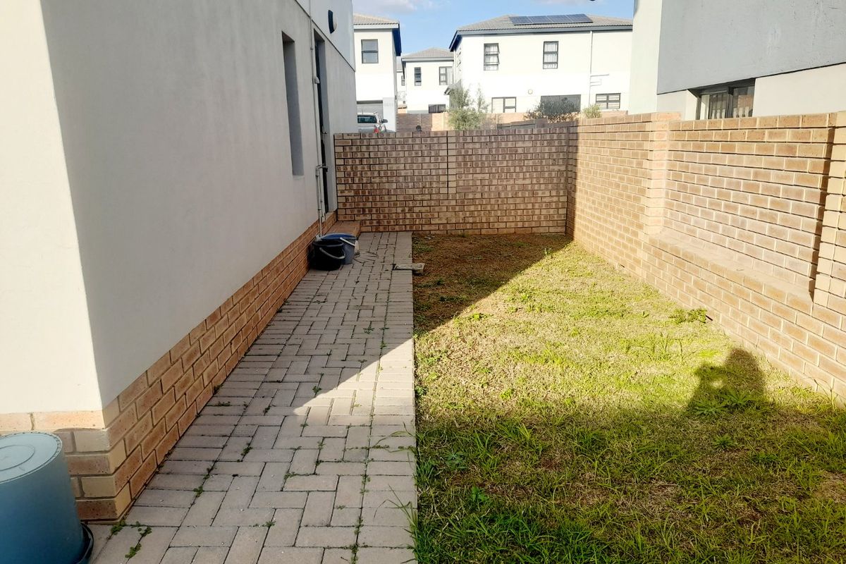 A side garden area featuring a paved walkway, brick boundary walls, and a small lawn section, offering potential for landscaping improvements.