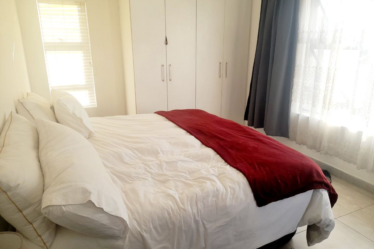 A bright bedroom featuring neutral tiled flooring, built-in cupboards, and natural light through venetian blinds.