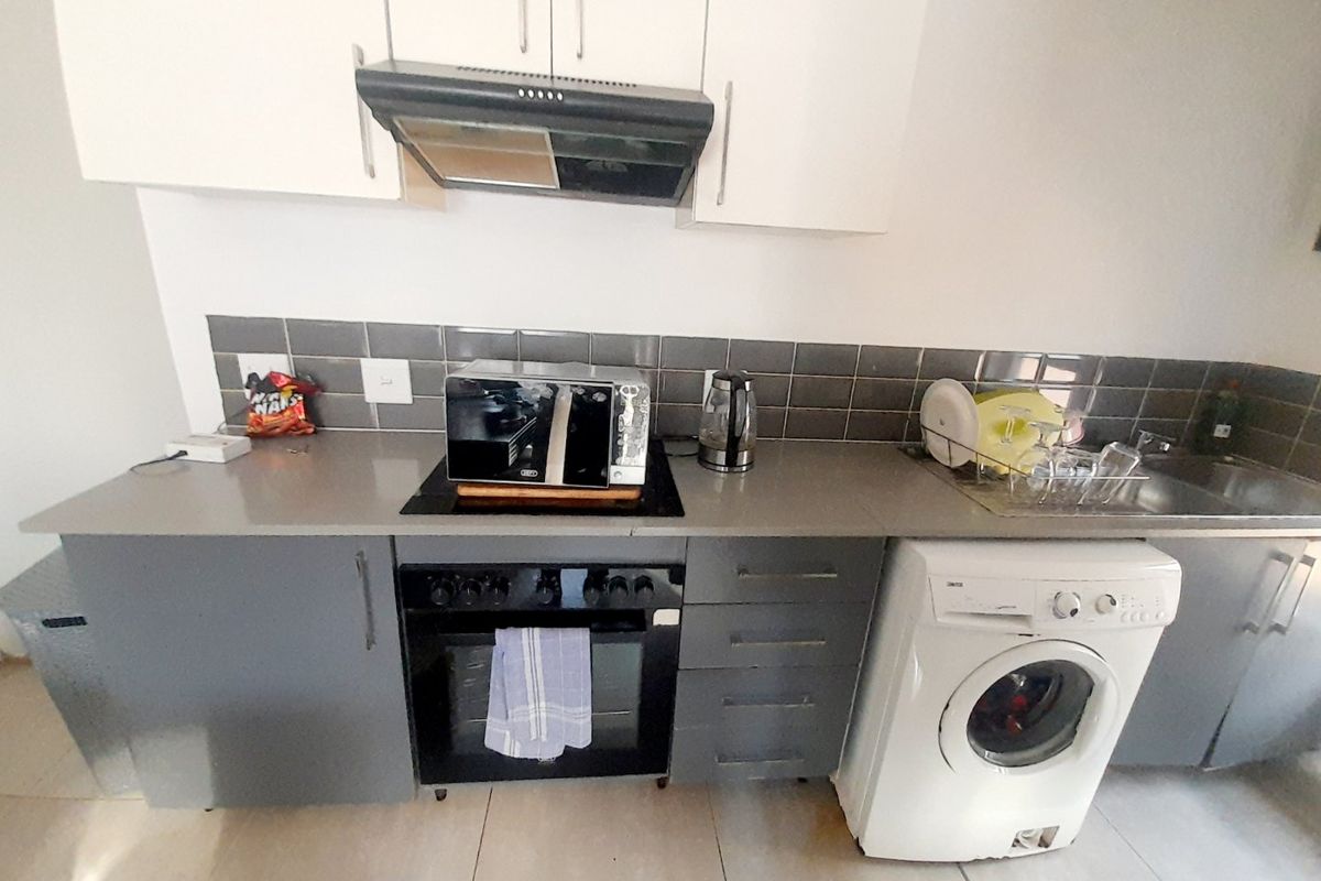 A functional kitchen featuring grey base cabinetry, white wall units, a built-in oven with hob, extractor fan, and tiled splashback.