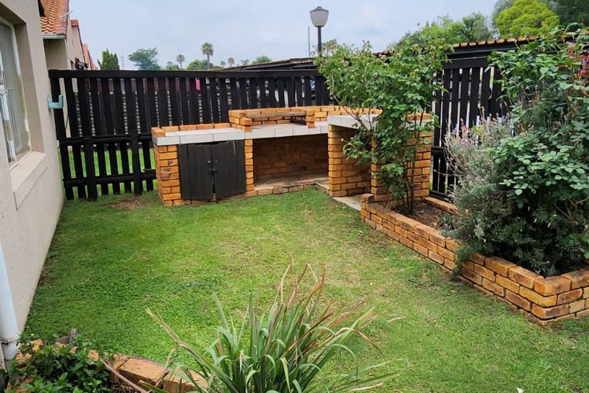A private rear garden featuring a built-in brick braai area, established garden beds with brick edging, and a perimeter timber fence.