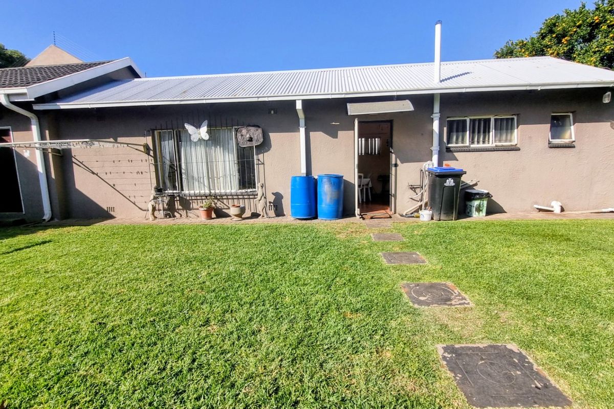 Rear view of the property featuring a lawn, paved pathway, and exterior wall with security bars on the windows.