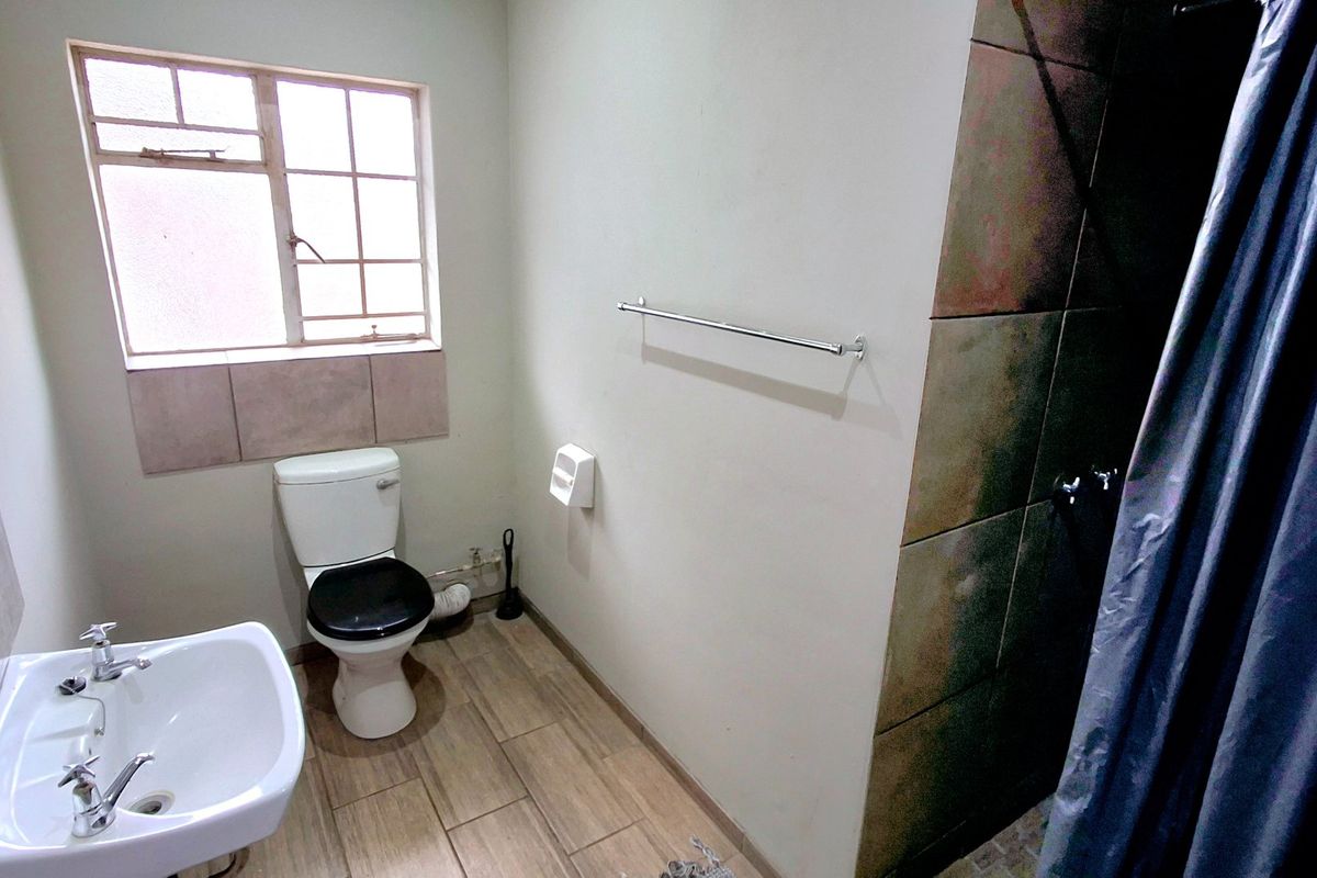 A functional bathroom featuring a pedestal basin, a standard toilet, and a shower enclosure with tiled walls and a curtain.