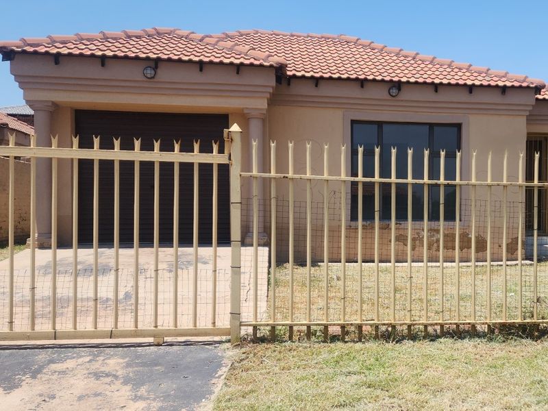 Front elevation of a single-story house featuring a tiled roof, integrated garage, and metal security fencing.