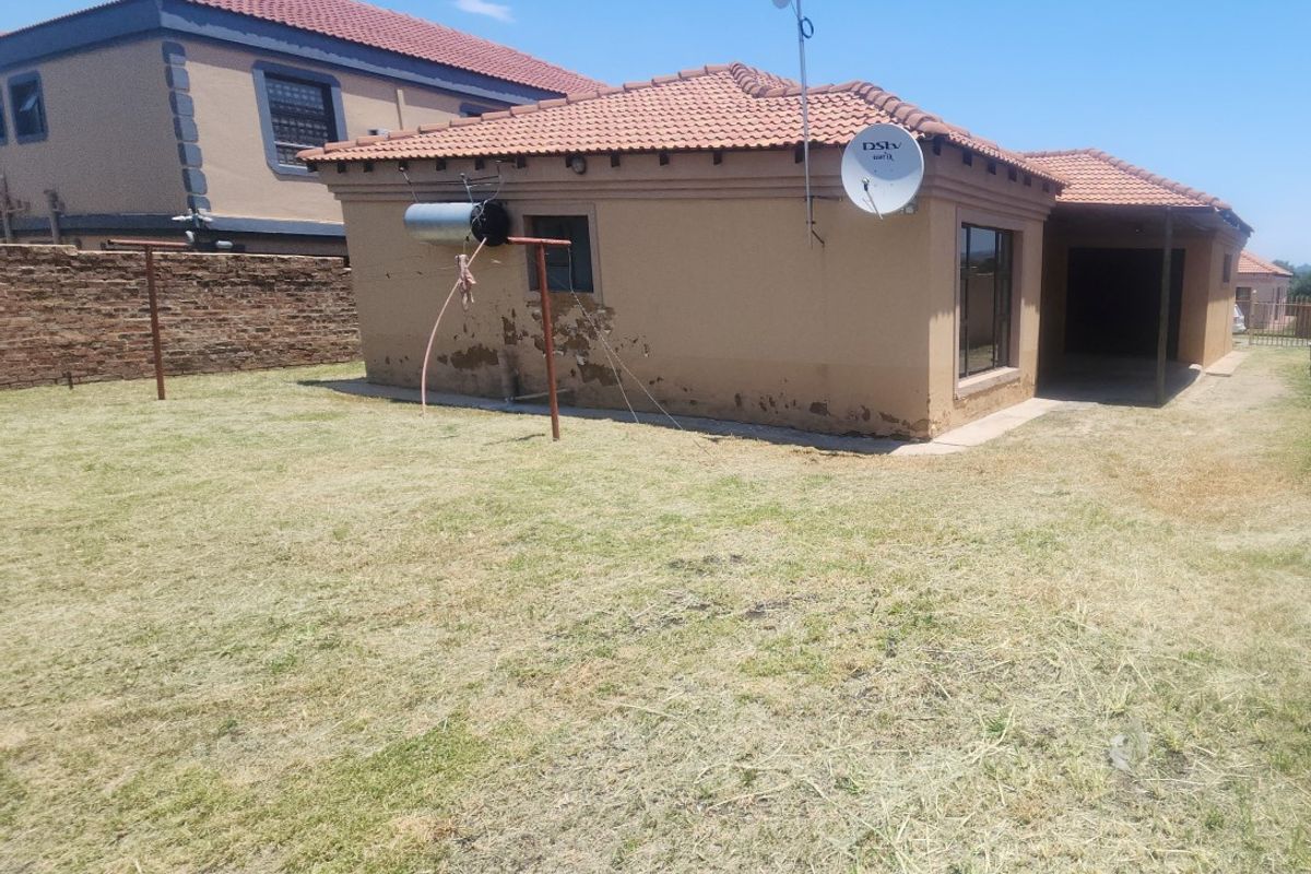 Rear view of the property showing a tiled roof, satellite dish, and a lawn area with visible exterior wall plaster deterioration.