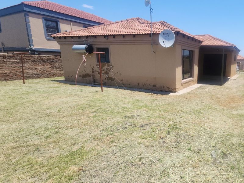 Rear view of the property showing a tiled roof, satellite dish, and a lawn area with visible exterior wall plaster deterioration.