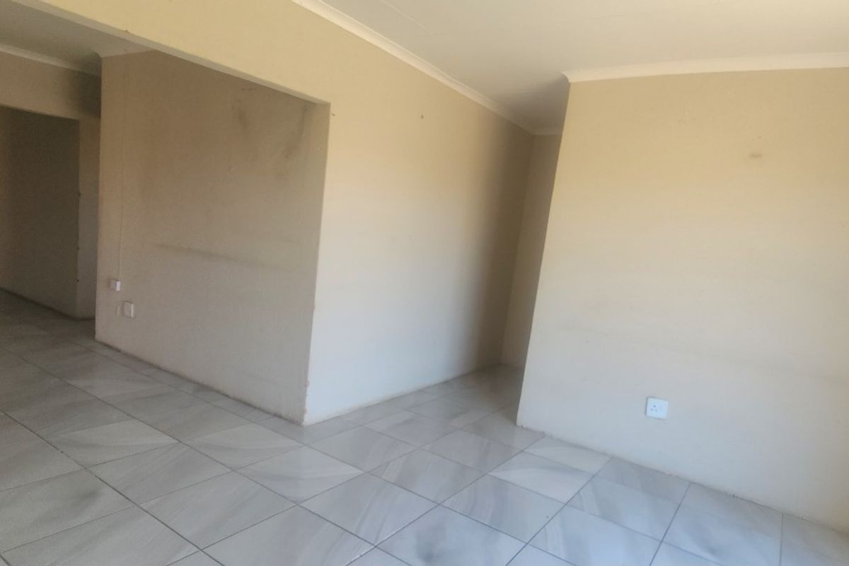 An empty, open-plan living area featuring neutral tiled flooring and coved ceilings, offering a blank canvas for interior design.