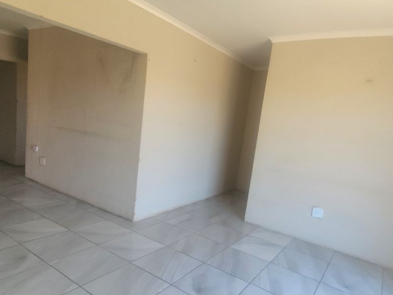 An empty, open-plan living area featuring neutral tiled flooring and coved ceilings, offering a blank canvas for interior design.