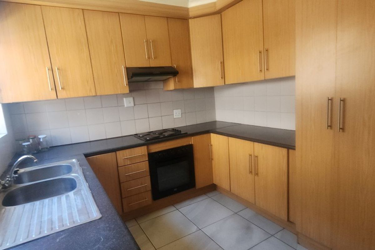 A functional kitchen featuring light wood-finish cabinetry, built-in oven, gas hob, extractor fan, and tiled flooring with ample storage space.