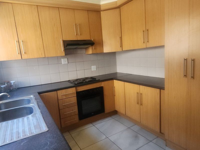 A functional kitchen featuring light wood-finish cabinetry, built-in oven, gas hob, extractor fan, and tiled flooring with ample storage space.