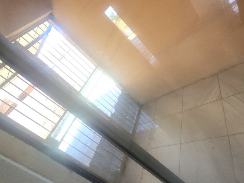 A small, tiled balcony area featuring security bars and a sliding door, captured from an angled perspective.