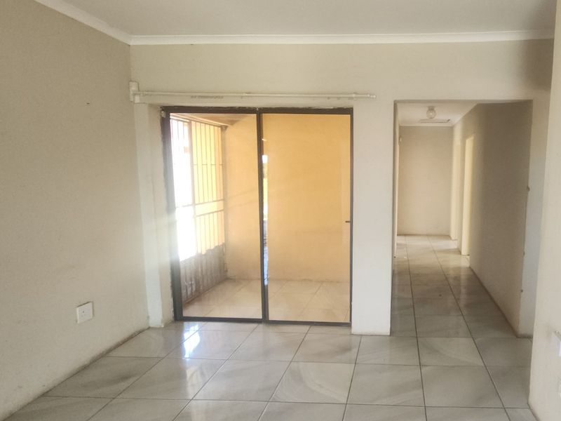 An empty living room featuring tiled flooring and a sliding glass door leading to an outdoor area, with a hallway leading to other rooms.