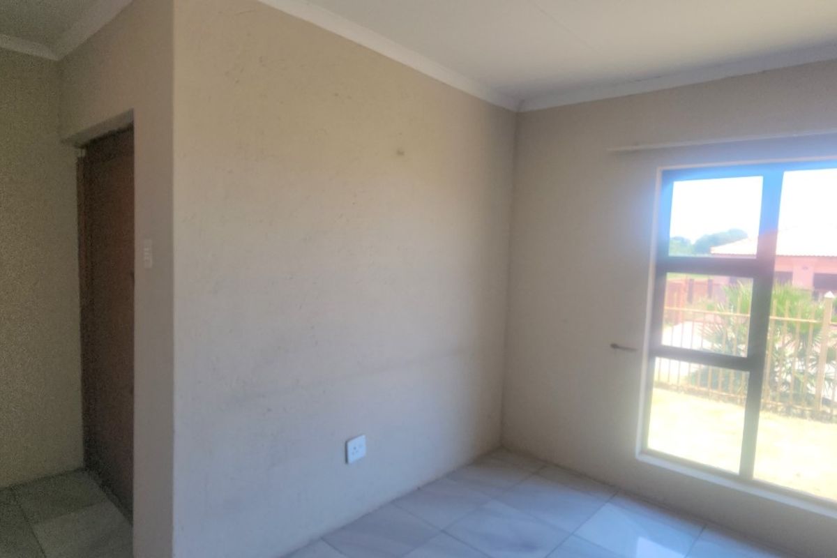 A vacant bedroom featuring tiled flooring, neutral wall finishes, and a large aluminium-framed window providing natural light.