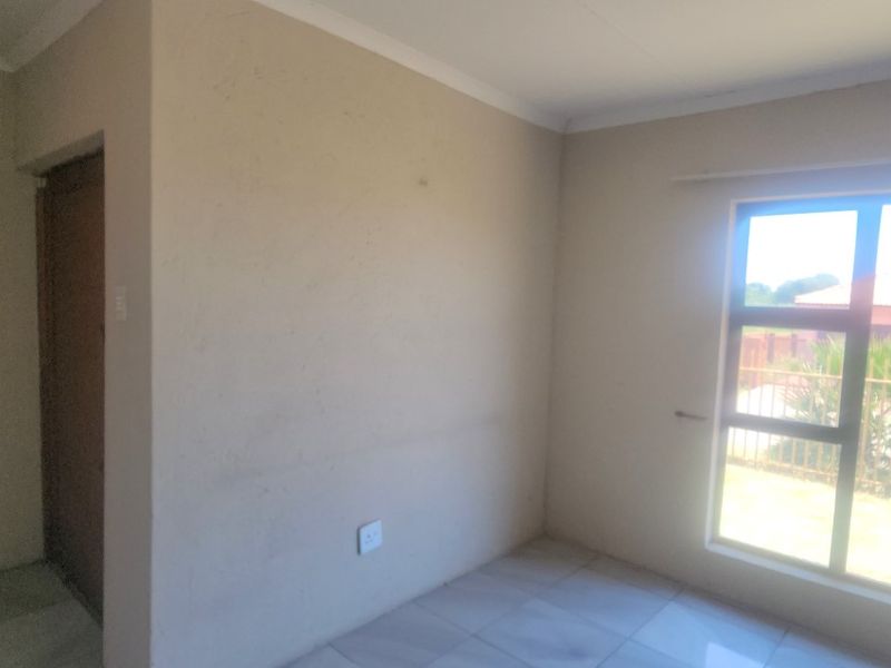A vacant bedroom featuring tiled flooring, neutral wall finishes, and a large aluminium-framed window providing natural light.