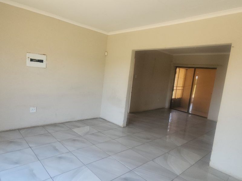 An empty, open-plan living area featuring neutral tiled flooring, plain walls, and a sliding glass door leading to an outdoor space.