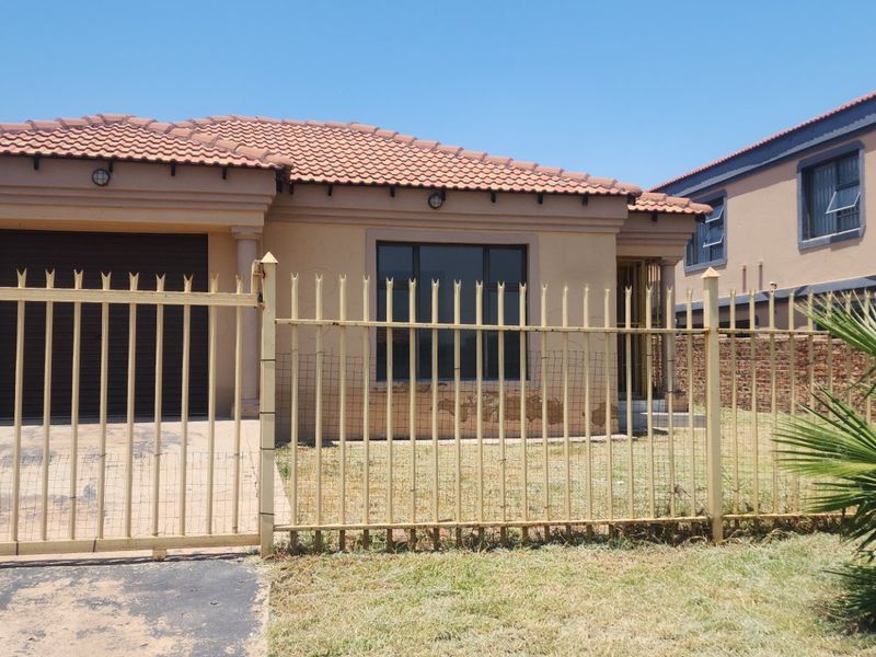 Front view of a single-story house featuring a tiled roof, integrated garage, and metal perimeter fencing with a concrete driveway.
