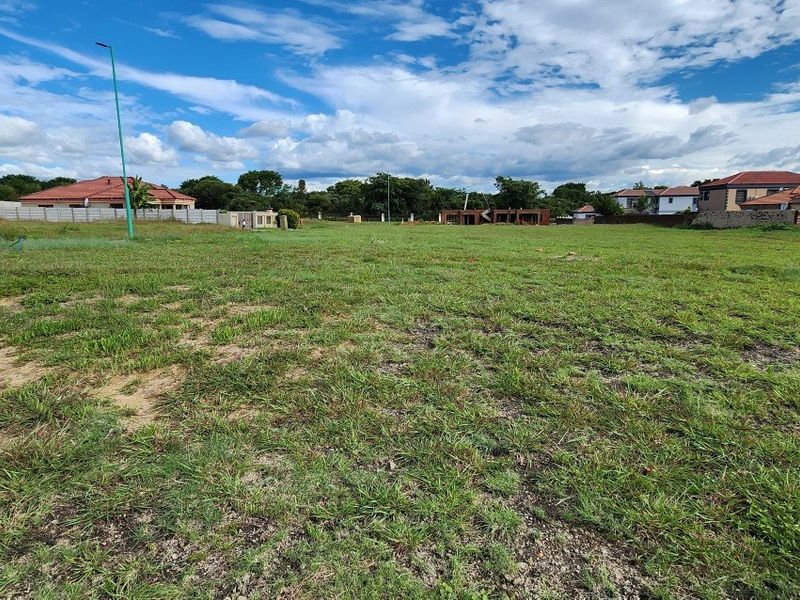 A wide-angle view of a vacant residential plot featuring a grass lawn and surrounding perimeter walls in a developed neighborhood.