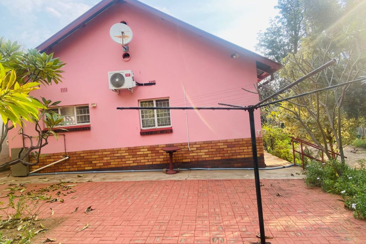 Rear exterior view of the house featuring a paved patio area, brick base detailing, and wall-mounted air conditioning unit.