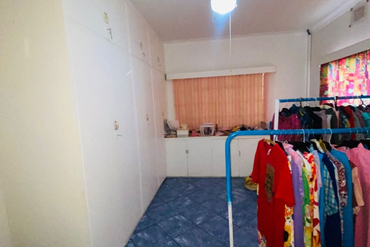 A bedroom featuring extensive built-in cupboard storage, tiled flooring, and a ceiling fan, offering functional space with potential for modernization.