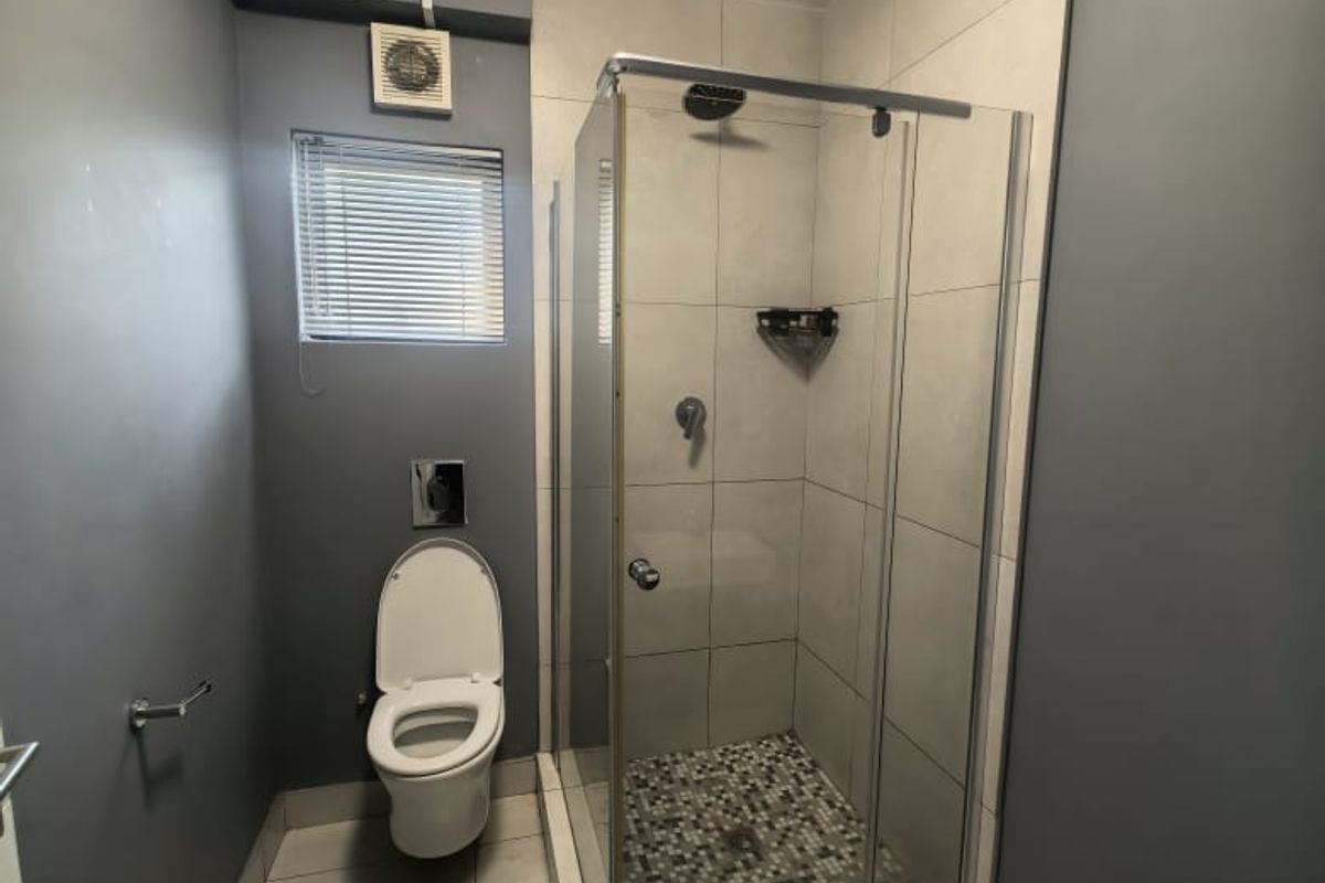 Modern bathroom featuring a glass-enclosed shower, wall-mounted toilet, and neutral tiled finishes with contemporary grey wall accents.