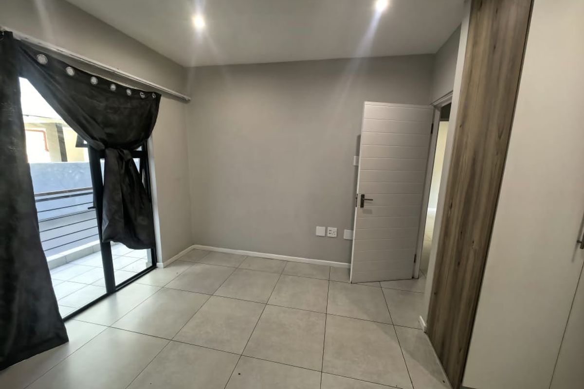 A bright, empty bedroom featuring modern tiled flooring, built-in cupboards, and a sliding glass door providing access to a private balcony.