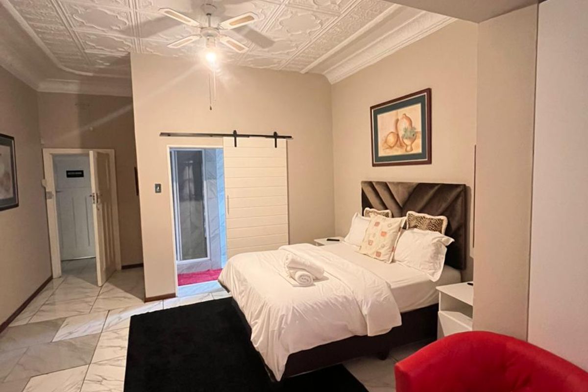 Spacious bedroom featuring decorative ceiling tiles, a ceiling fan, marble-look tiled flooring, and a sliding barn door leading to an en-suite bathroom.