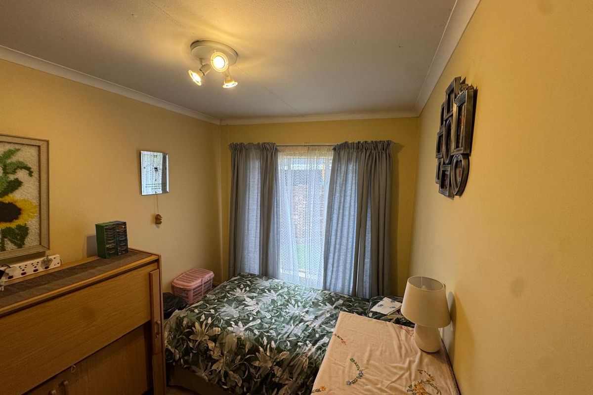 A standard bedroom featuring yellow walls, a central ceiling light fixture, and a window with curtains.