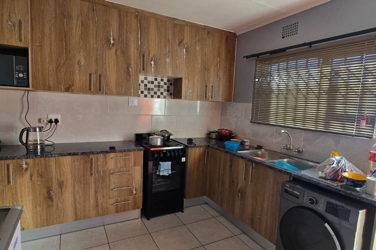 Functional kitchen featuring wood-look laminate cabinetry, granite countertops, tiled backsplash, and integrated space for laundry appliances with direct garden access.