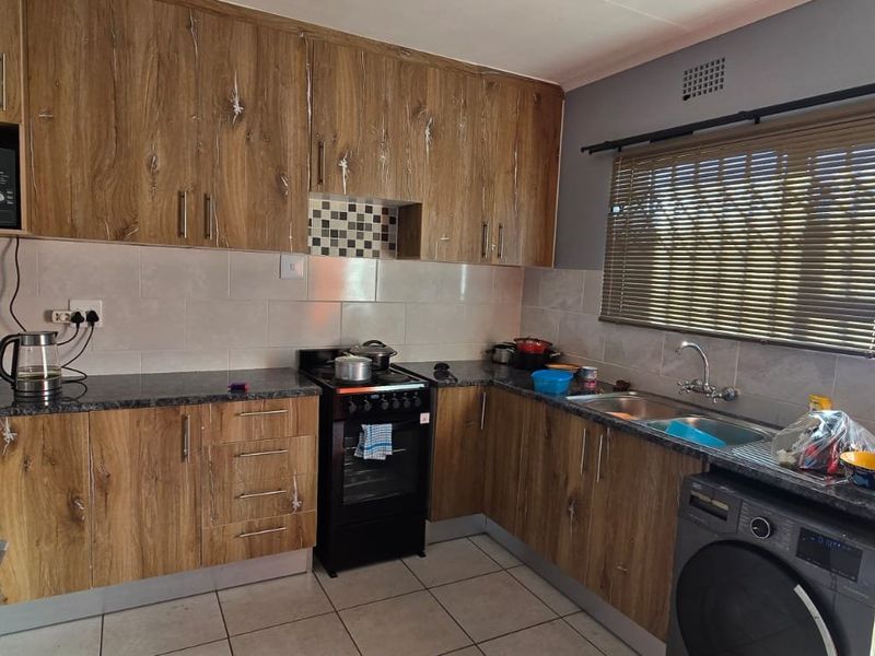 Functional kitchen featuring wood-look laminate cabinetry, granite countertops, tiled backsplash, and integrated space for laundry appliances with direct garden access.
